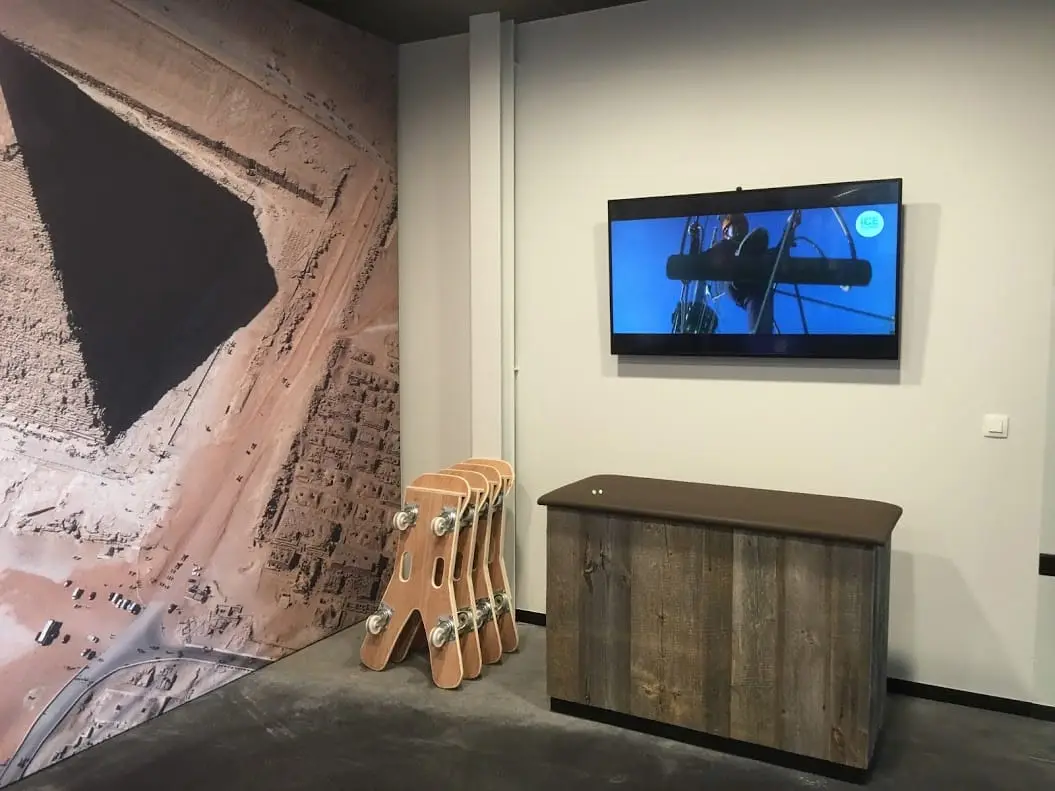 Een groot scherm aan de muur van een kantoor, naast een houten wandkast